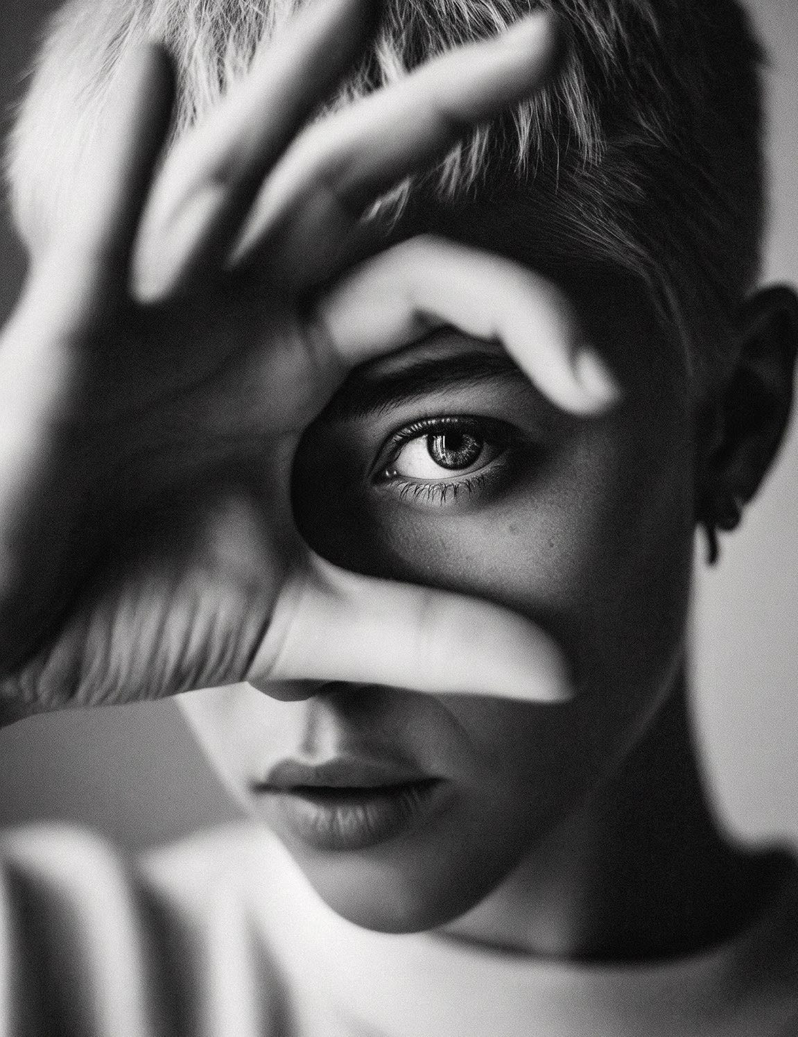 Retrato em preto e branco de uma mulher olhando pelo vão entre os dedos